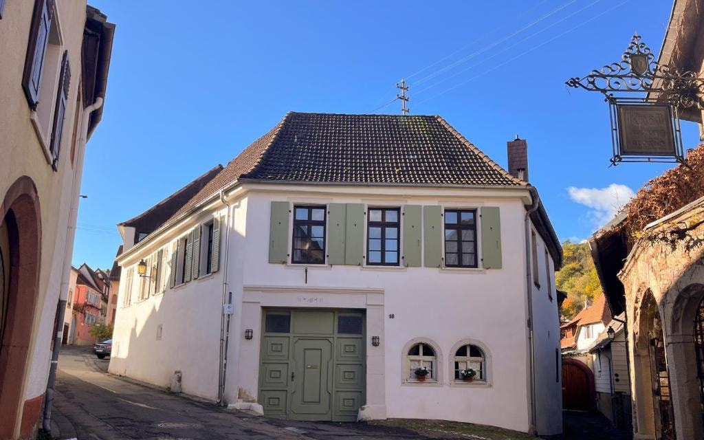 Das Haus von der Straße: weiße Fassade, grüne Läden, grünes Hoftor, über der Tür die Nummer 18